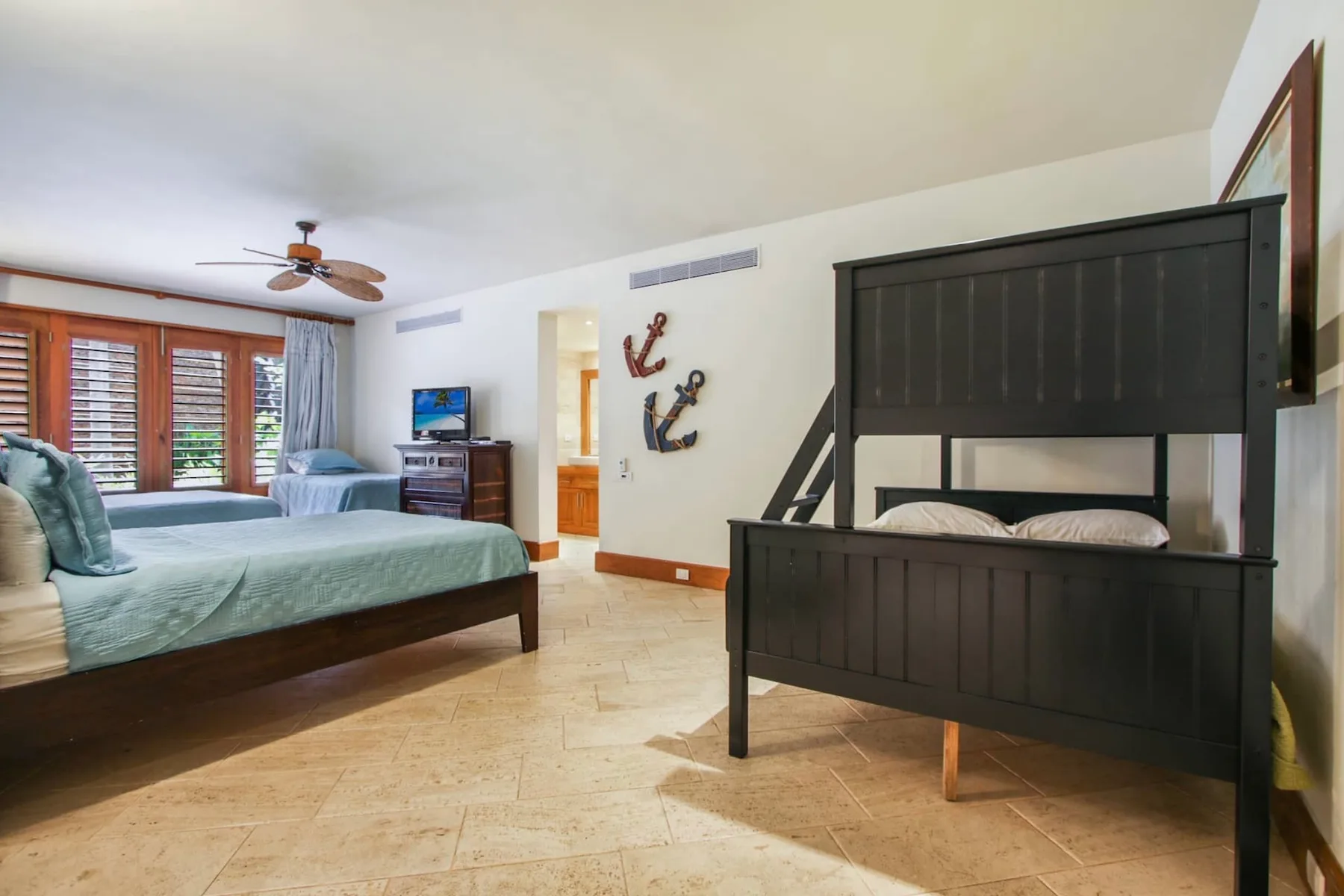 A bedroom with two beds, a television, and wood shutters.