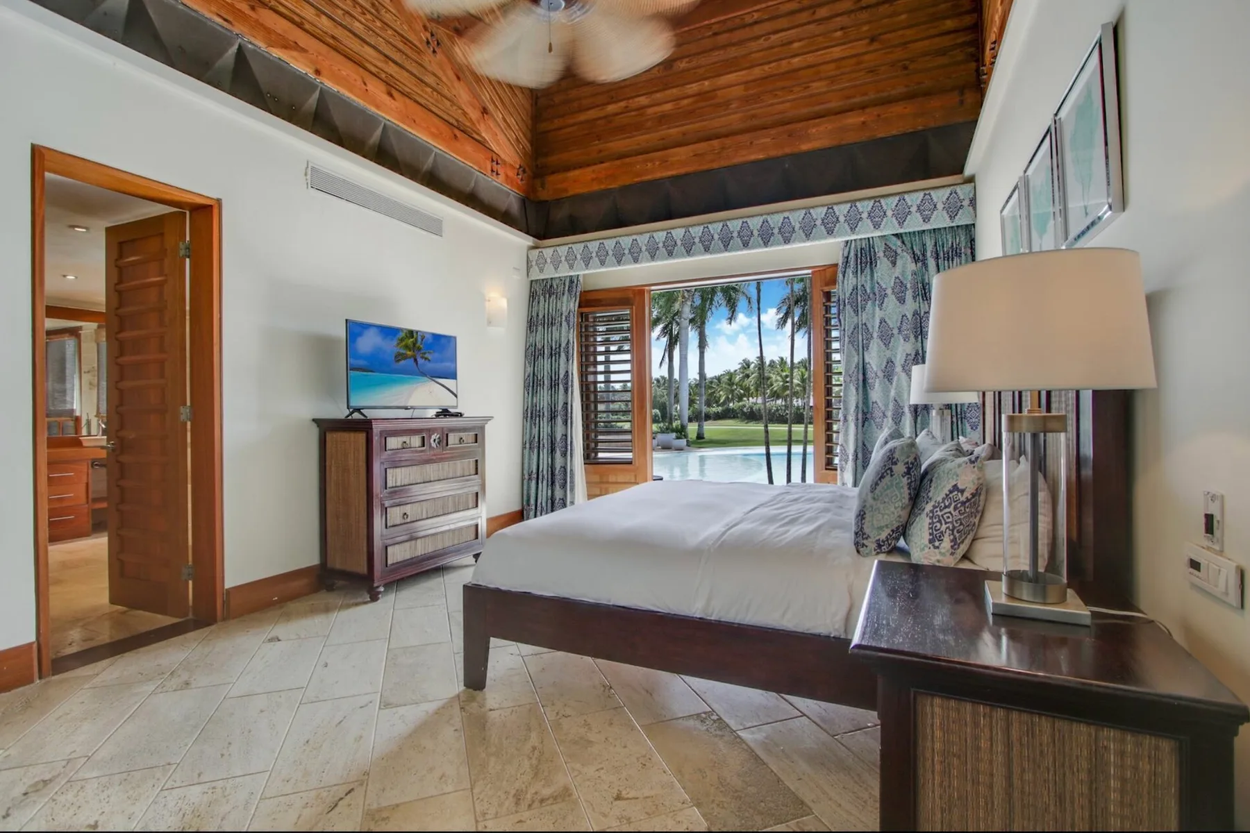 A bedroom with a bed, a wooden ceiling, and glass doors opening to a garden.