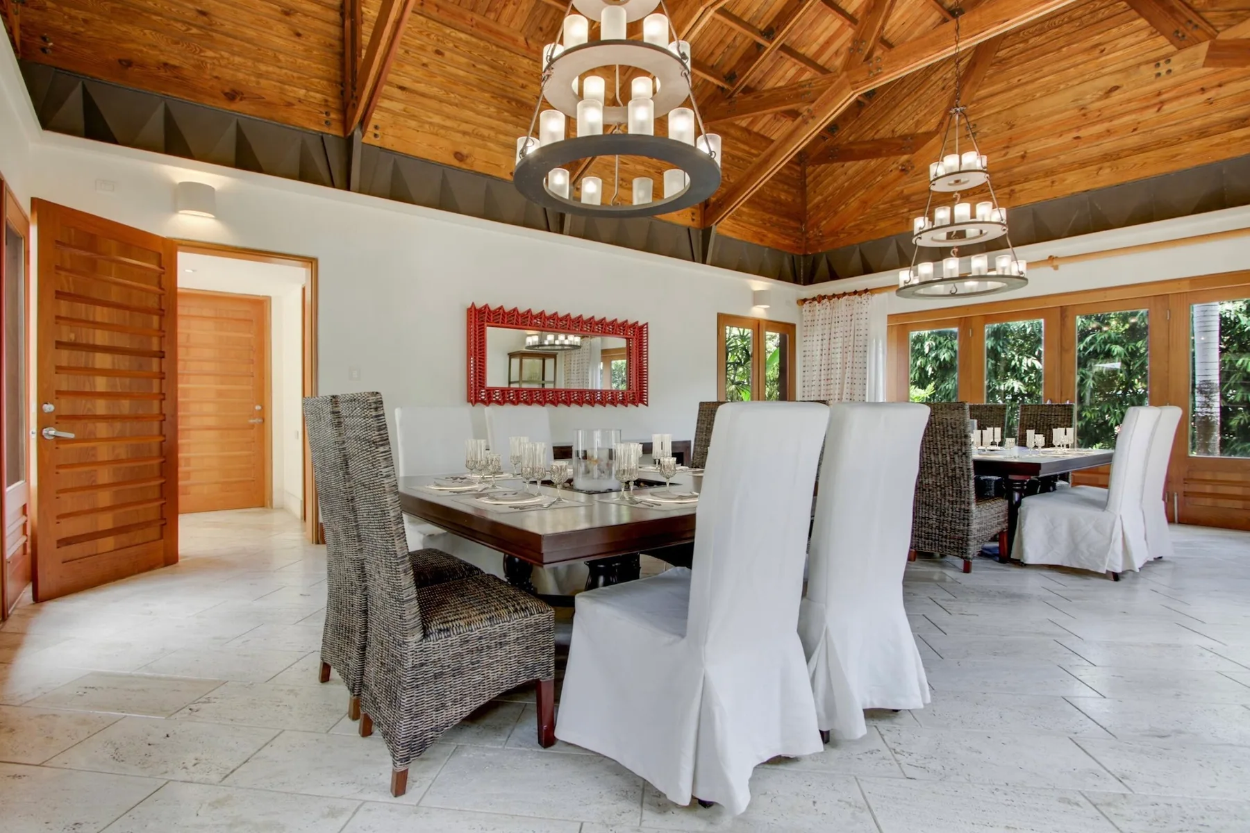 A dining room with a long table beneath wooden ceiling beams and hanging lights.