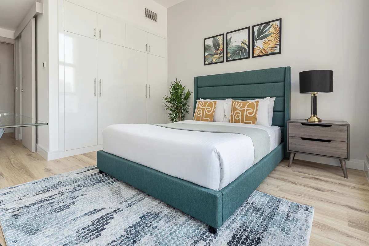 Un dormitorio con una cama tapizada en verde azulado, ropa de cama blanca y láminas botánicas enmarcadas.