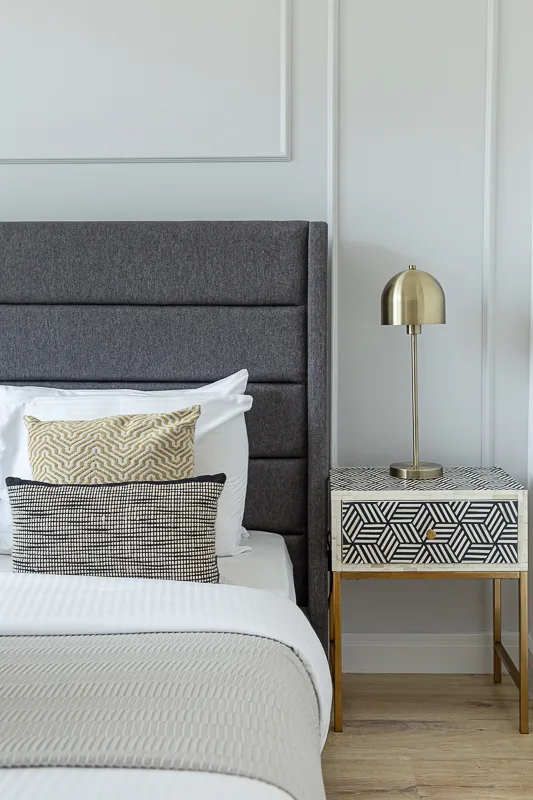 Un dormitorio con una cama bien tendida y una mesa auxiliar con una lámpara.