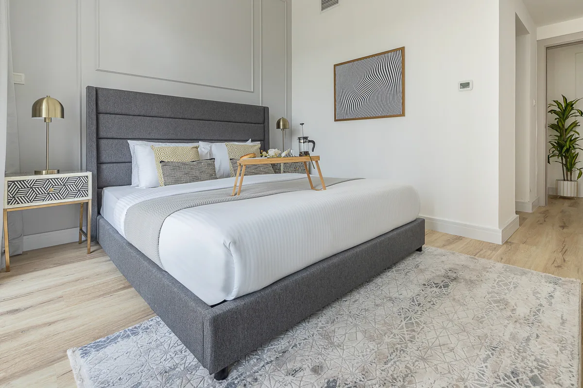 Un dormitorio con una cama bien tendida, mesitas de noche y una alfombra estampada.