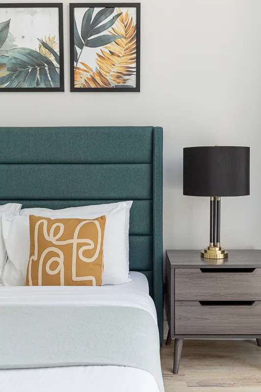 Un dormitorio con una cama tapizada en verde azulado, ropa de cama blanca y una mesita de noche.