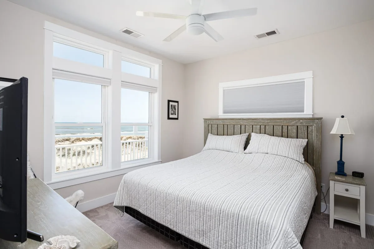 Un dormitorio luminoso con una cama junto a grandes ventanas con vistas al agua.