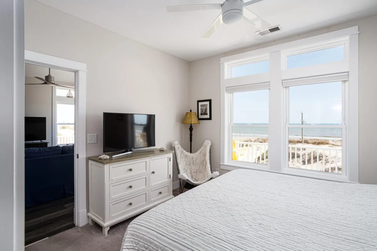 Un dormitorio luminoso con cama, cómoda y grandes ventanas con vistas al agua.