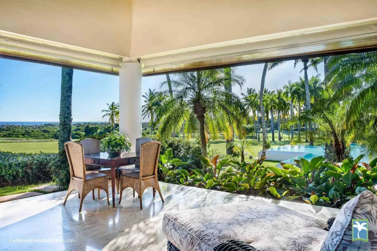Un patio cubierto da a un jardín con palmeras y una piscina.