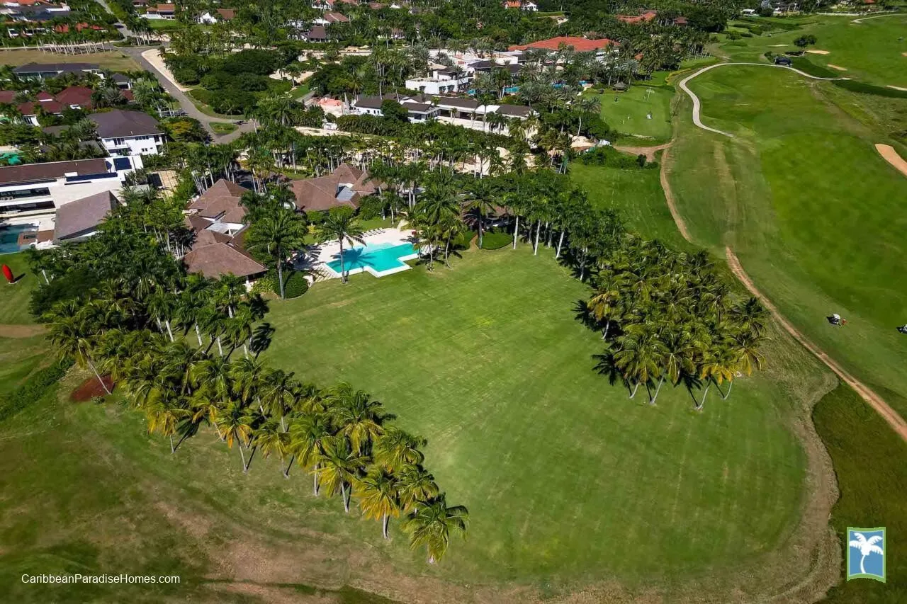 Vista aérea de una propiedad bordeada de palmeras junto a un amplio campo verde.