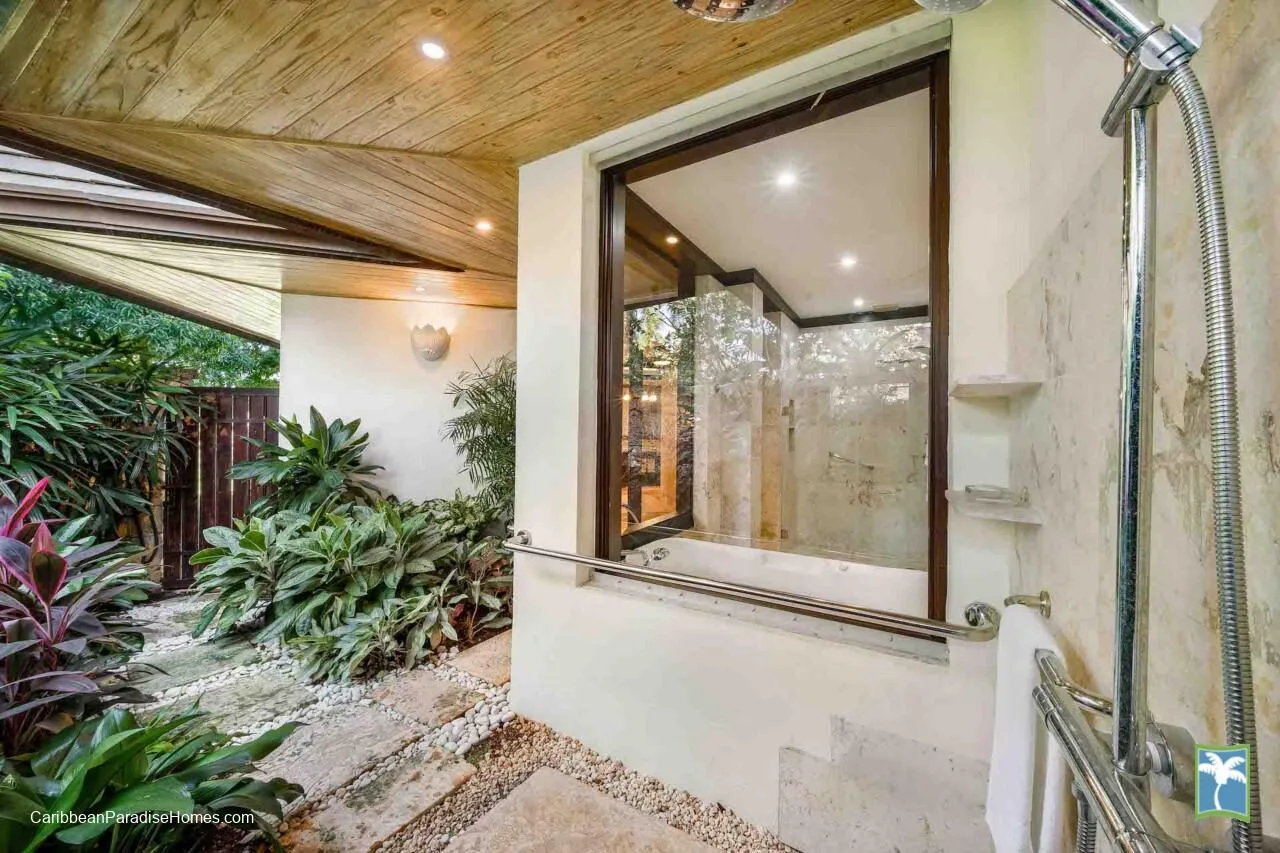 Un baño con una zona de ducha de vidrio junto a un jardín frondoso.