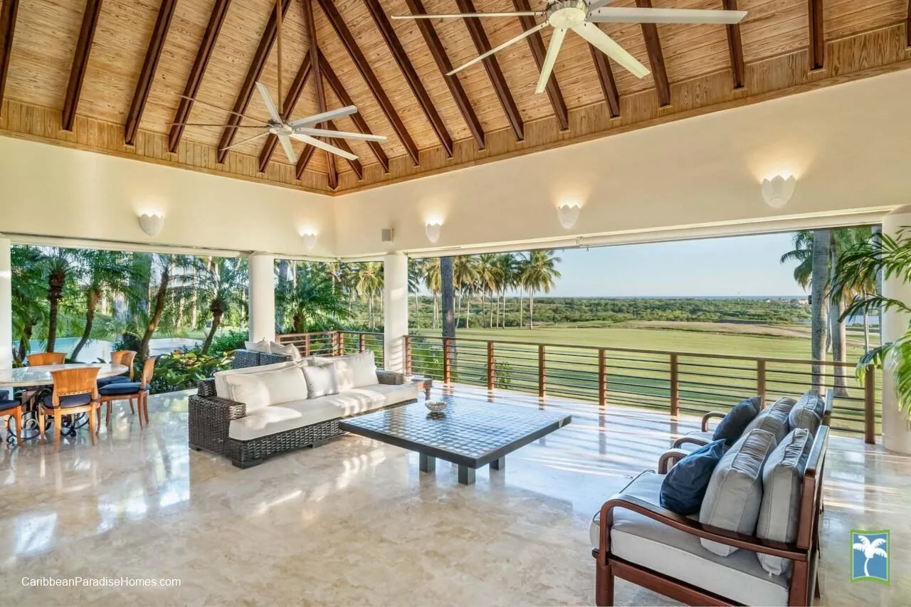 Una sala de estar abierta con asientos y una mesa baja frente a un paisaje tropical.