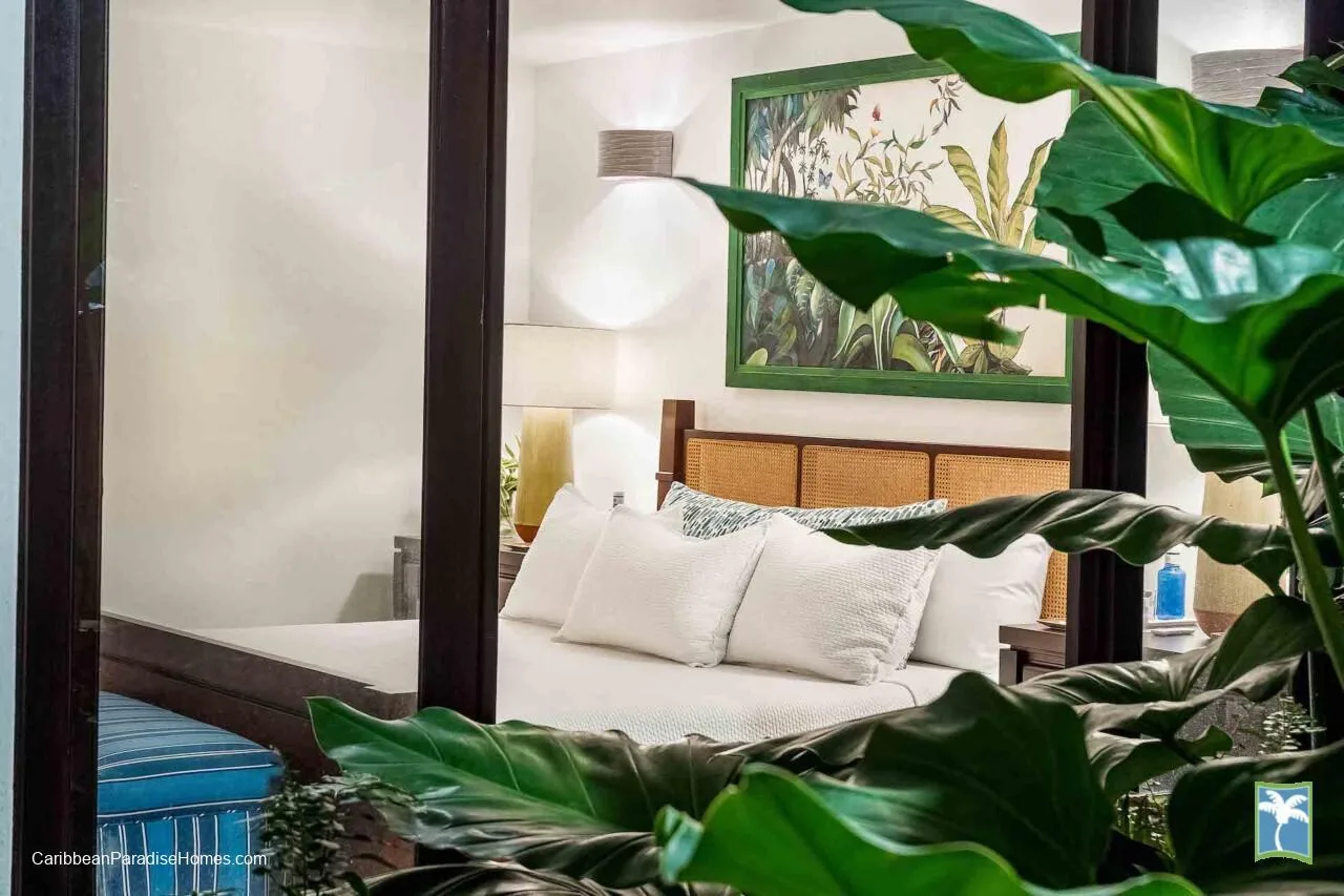 Un dormitorio con una cama, un cuadro botánico enmarcado y plantas frondosas en primer plano.