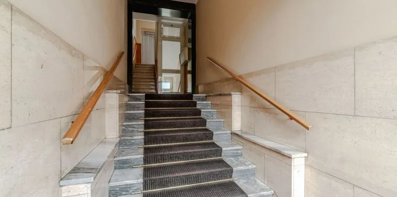 Una escalera revestida de azulejos, con peldaños oscuros y pasamanos de madera.