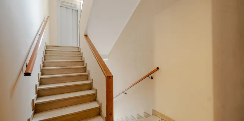 Una escalera con pasamanos de madera y peldaños de color claro.