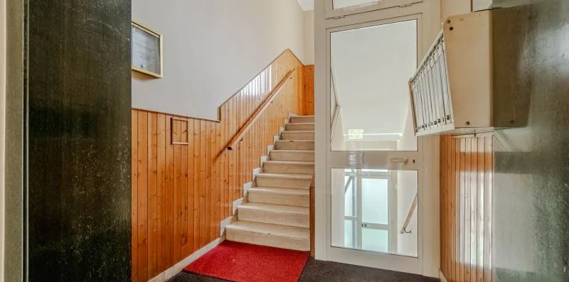 Una escalera interior con revestimiento de madera y una alfombra roja al pie.