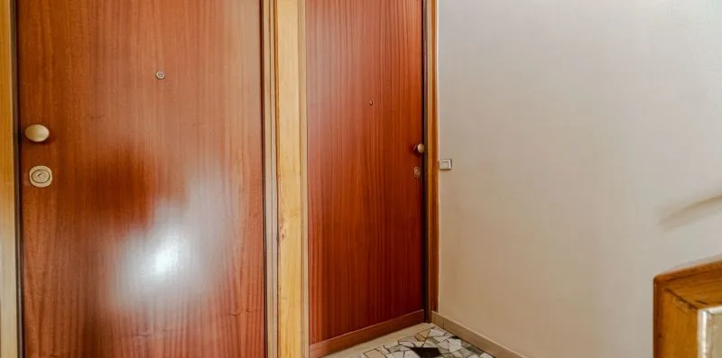 Un pasillo interior con puertas de madera y suelo de baldosas.
