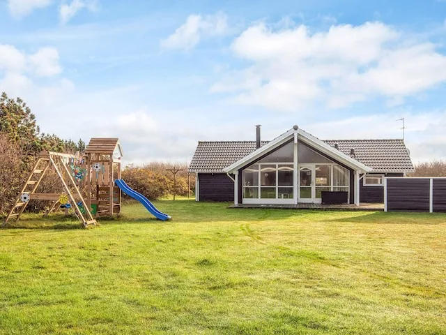 A vacation house stands beside a grassy yard and a children's play structure.