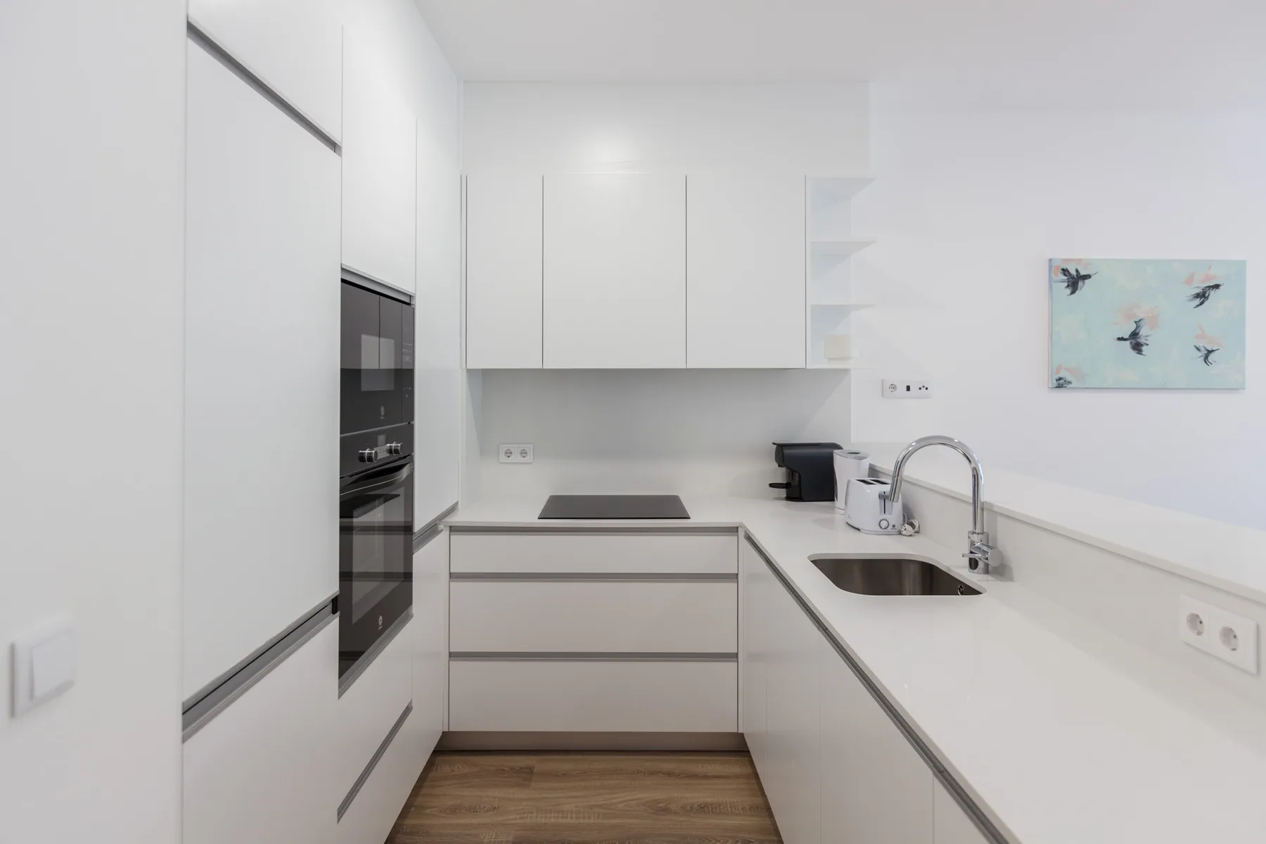 Una cocina moderna blanca con horno empotrado, placa de cocción y fregadero.