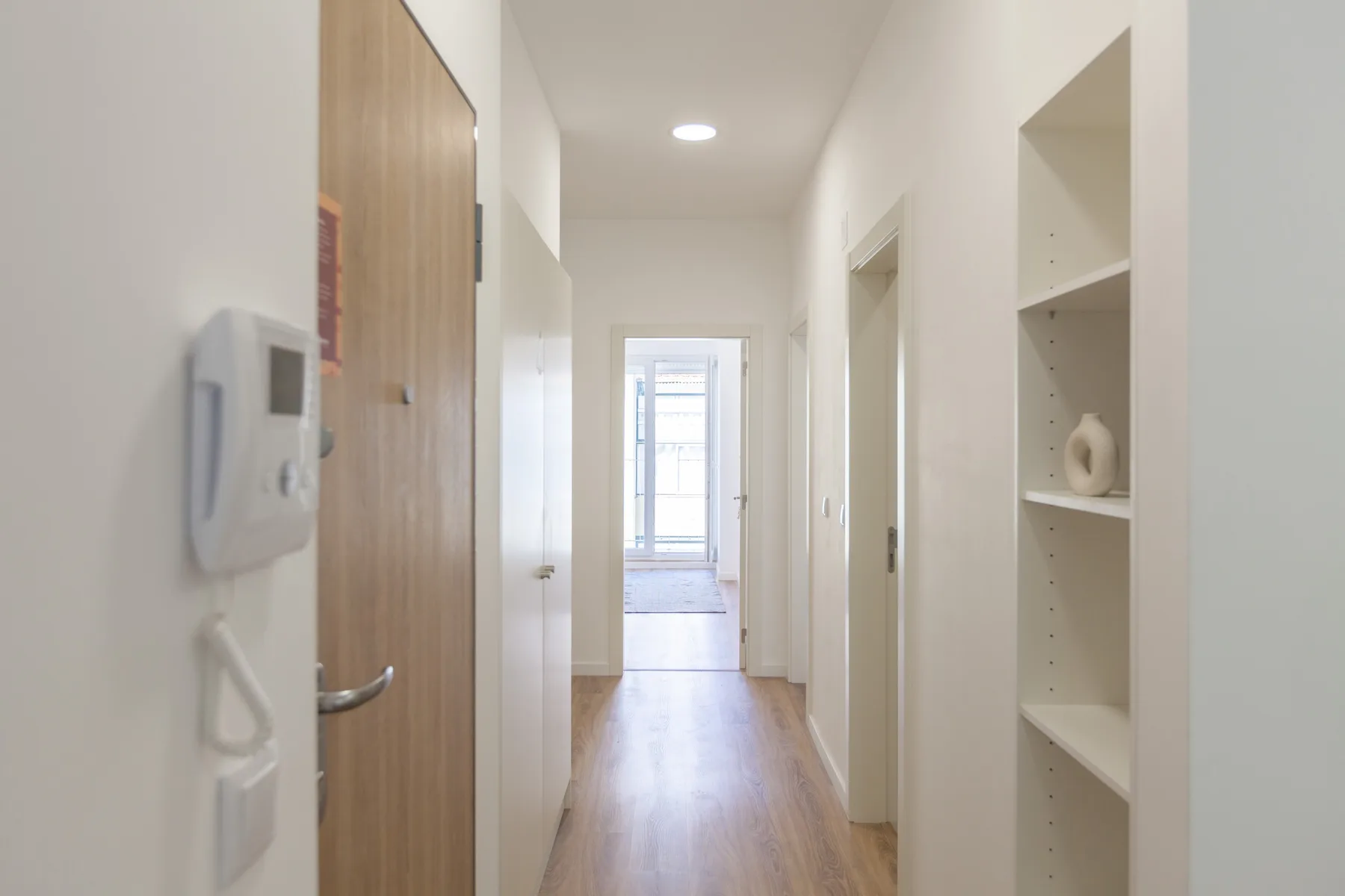 Un pasillo luminoso con suelo de madera y estanterías empotradas.