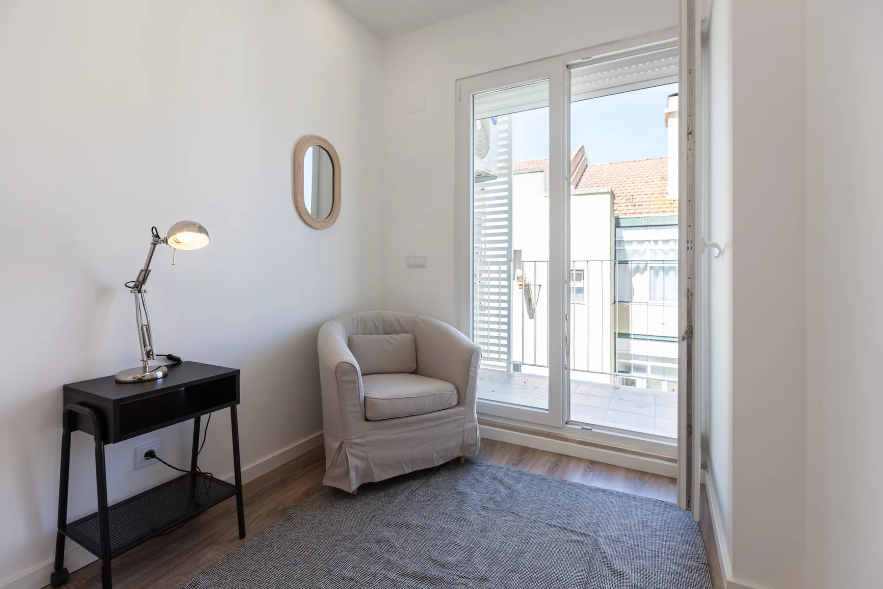 Una luminosa zona de estar con un sillón junto a una puerta de cristal al balcón.