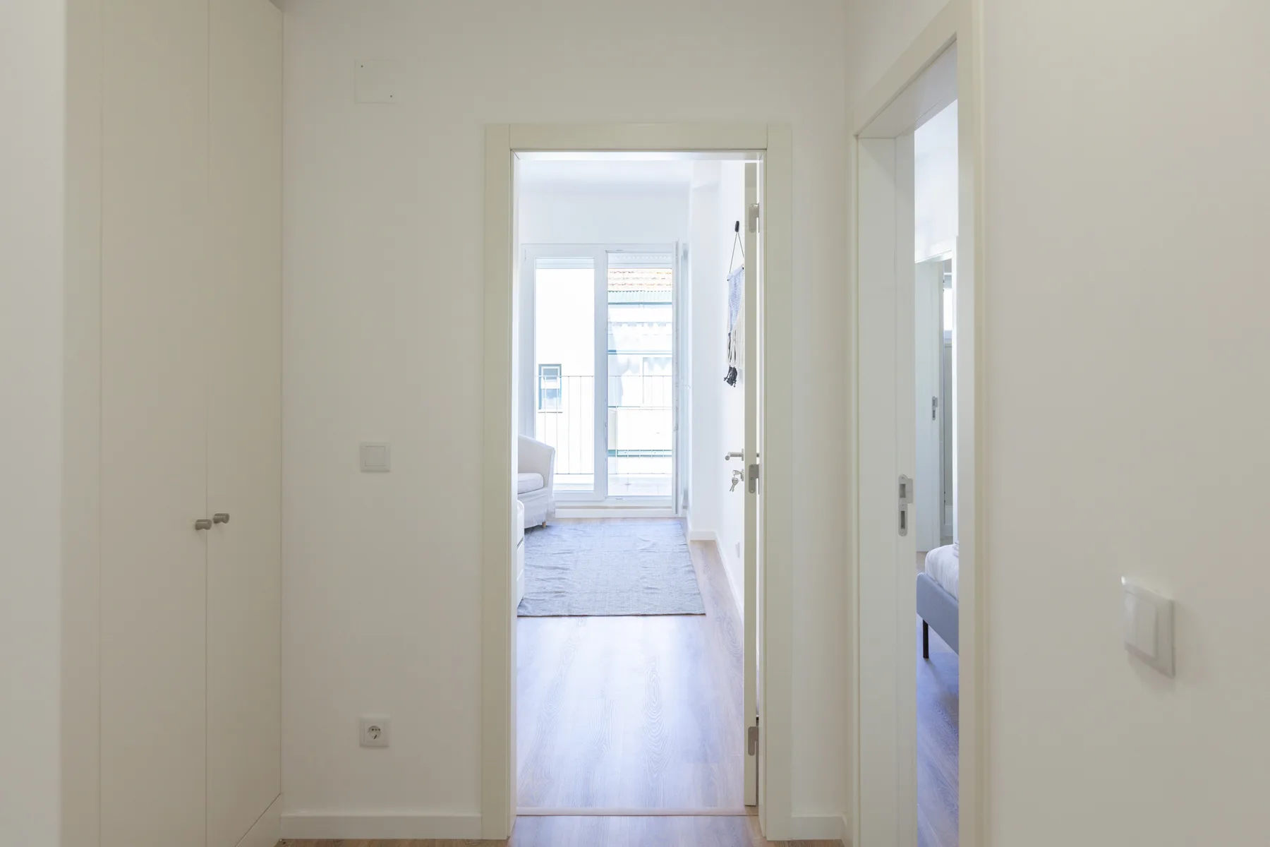 Un pasillo luminoso da a una habitación con ventanas grandes.