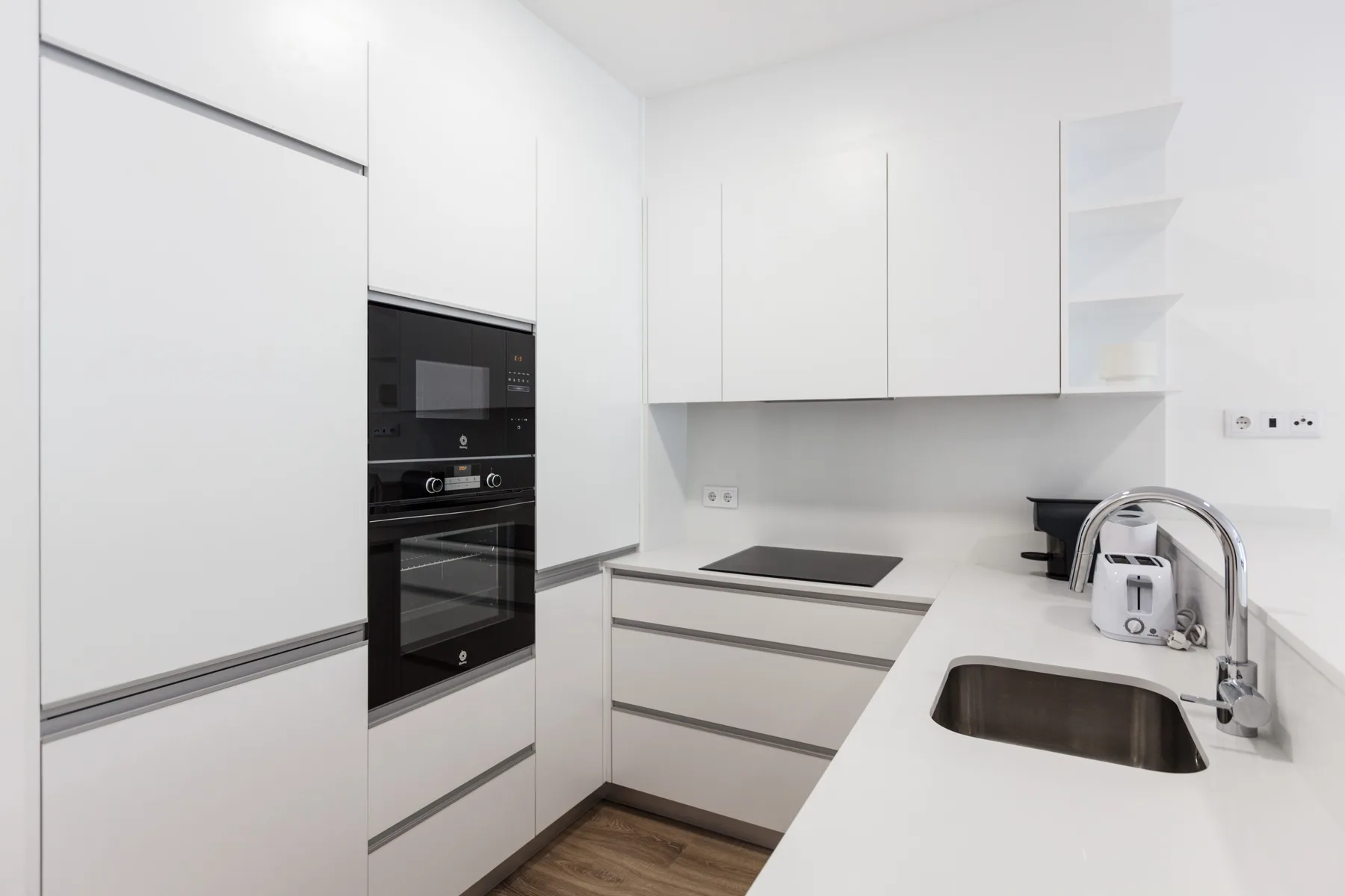 Una cocina moderna con armarios blancos, un horno empotrado y un fregadero oscuro.