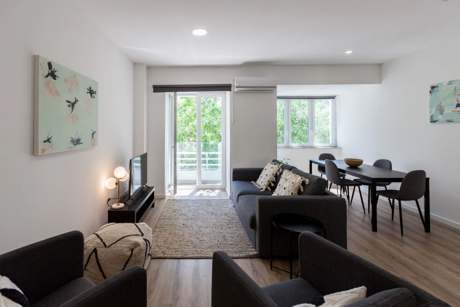Una sala de estar y comedor con asientos oscuros y una mesa junto a puertas de vidrio.