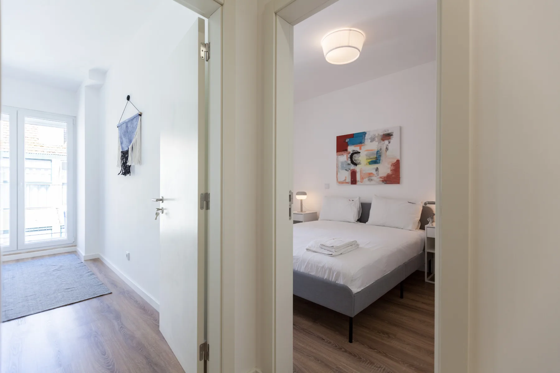 Se ve un dormitorio con una cama y una obra colorida a través de una puerta abierta.