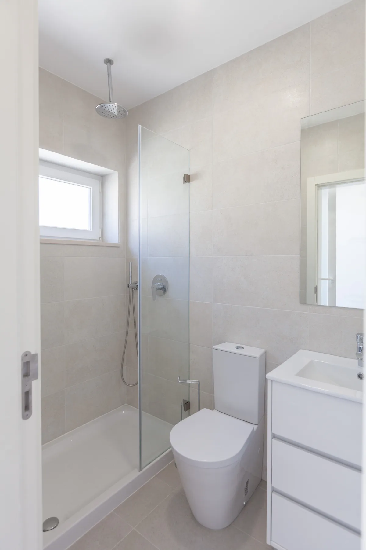 Un baño luminoso con ducha, inodoro y mueble de lavabo.