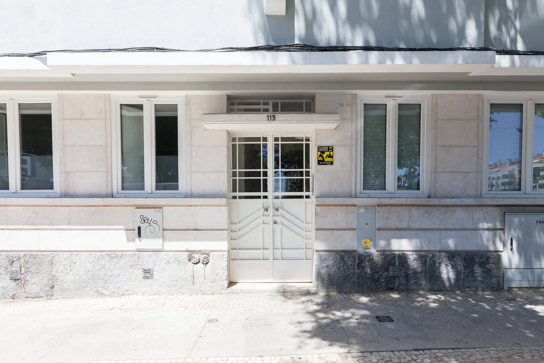 Entrada de edificio de apartamentos a la calle, con una puerta blanca y ventanas.