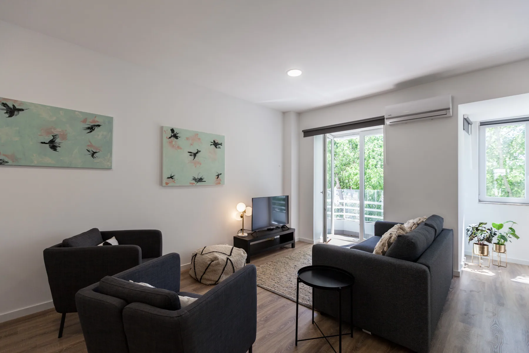 Sala de estar con asientos oscuros, una mesa de centro y grandes ventanas.