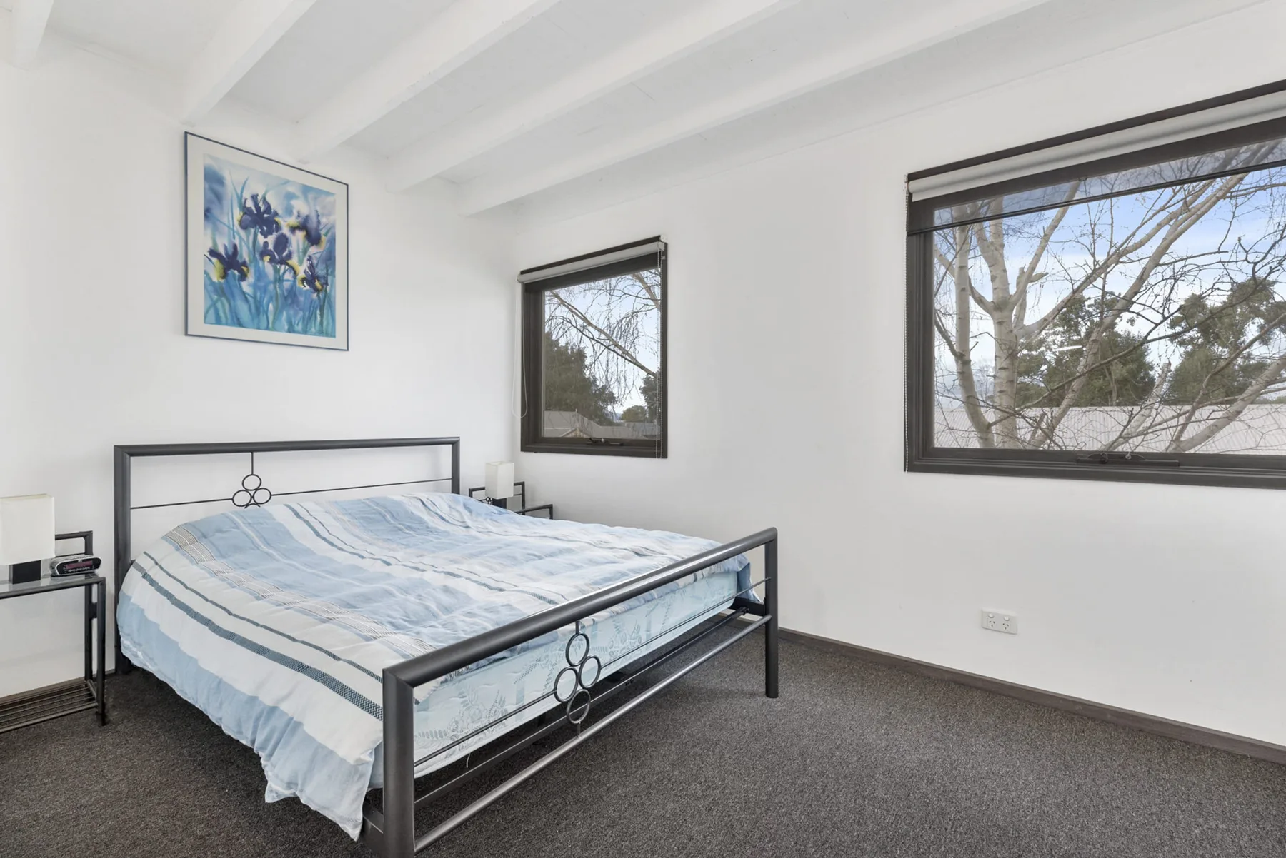A bright bedroom with a metal bed and large windows.