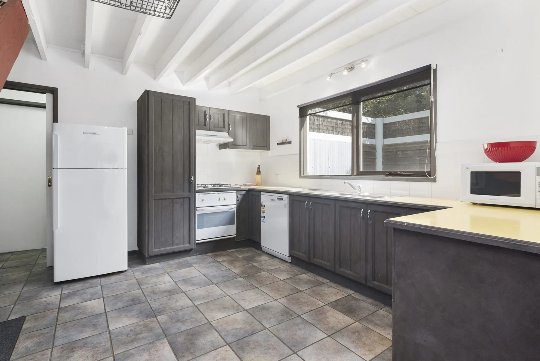 A kitchen with dark cabinets, white appliances, and a large window.