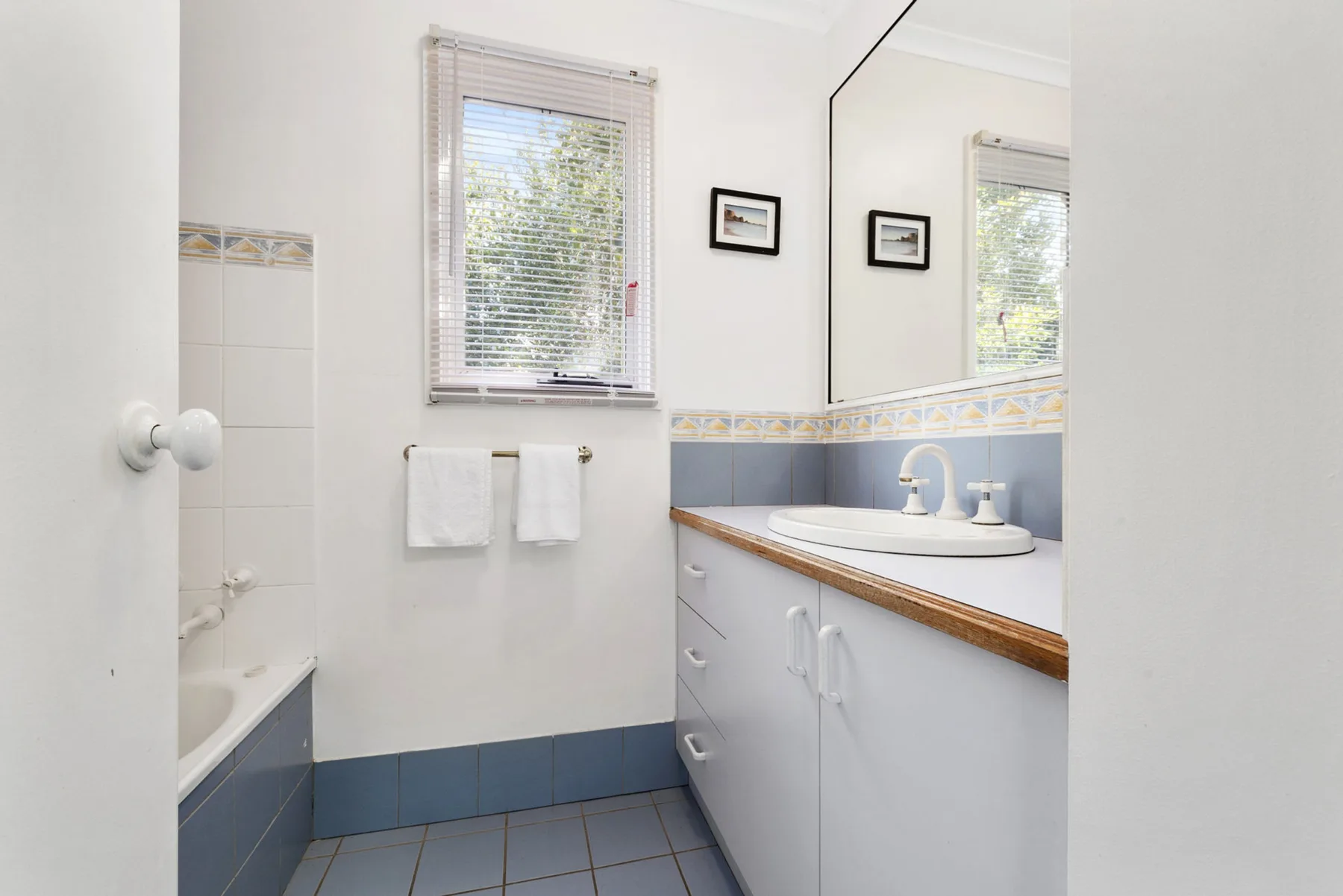 A bright bathroom with a sink vanity, mirror, and window.