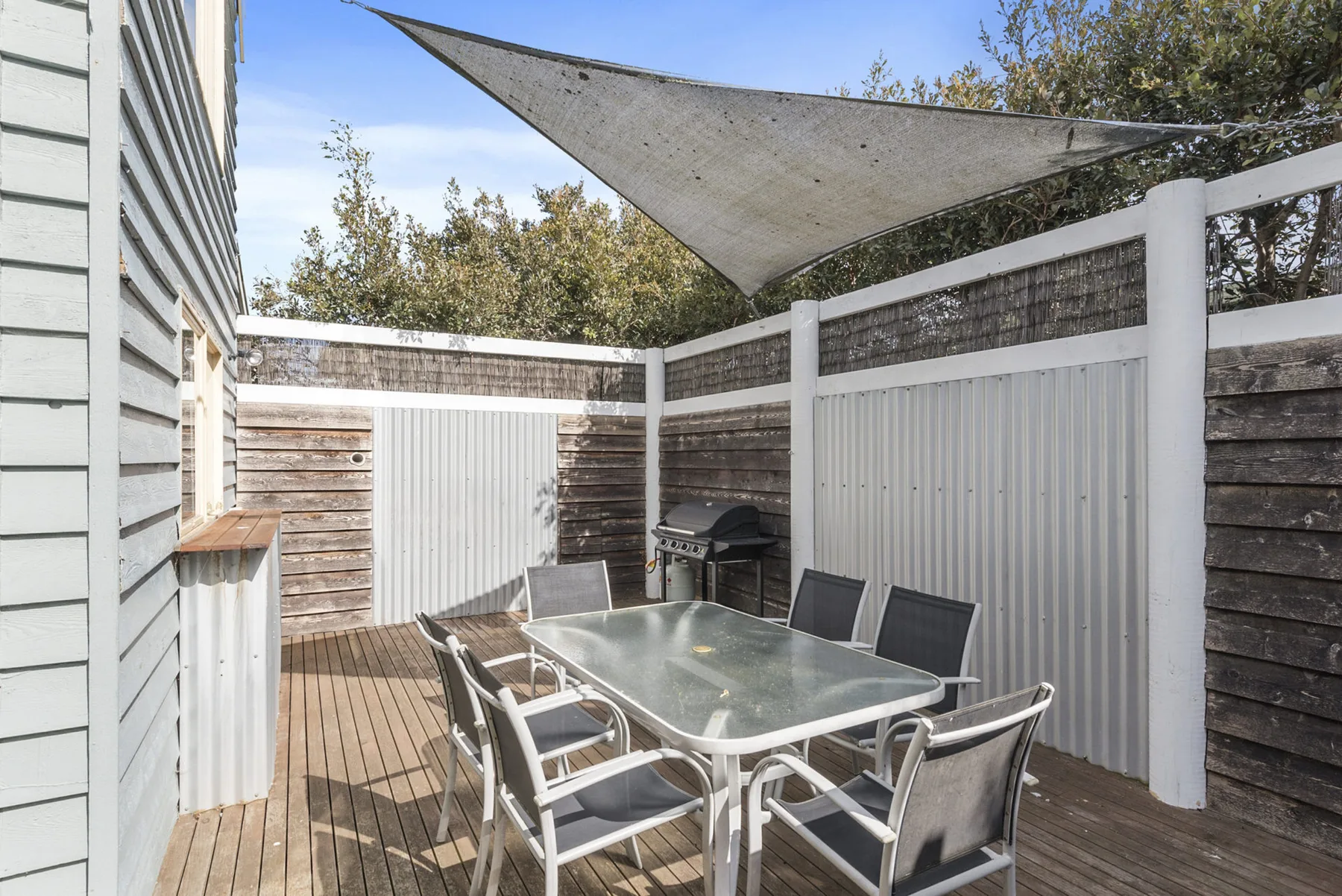 An outdoor dining area on a wooden deck, shaded by a fabric canopy.