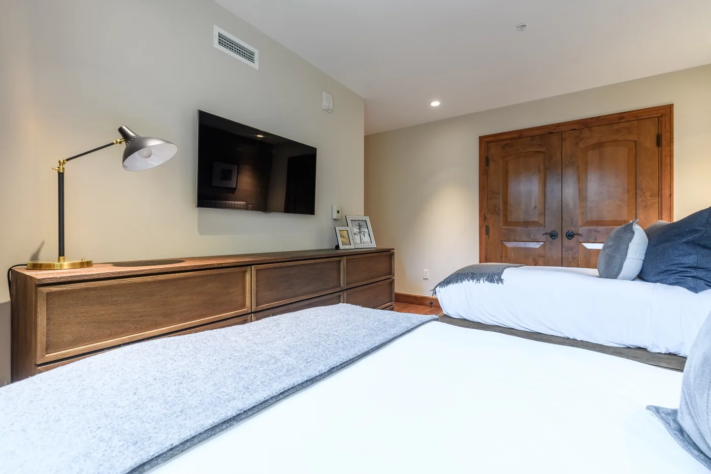 A bedroom with a bed, a wall-mounted television, and wooden doors.