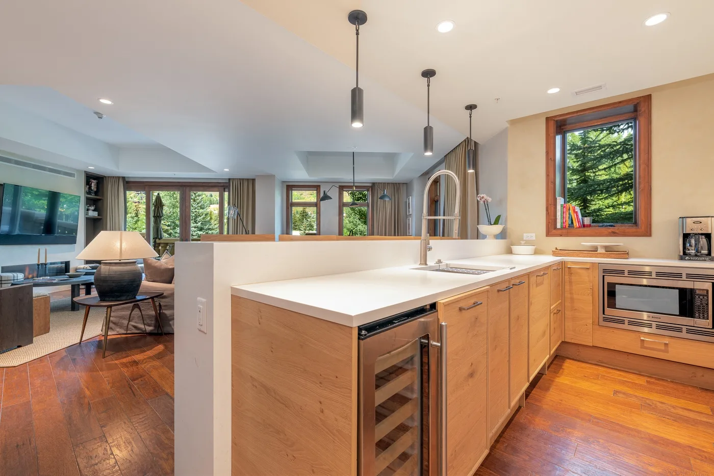 A modern kitchen with a wood island and large windows overlooking greenery.