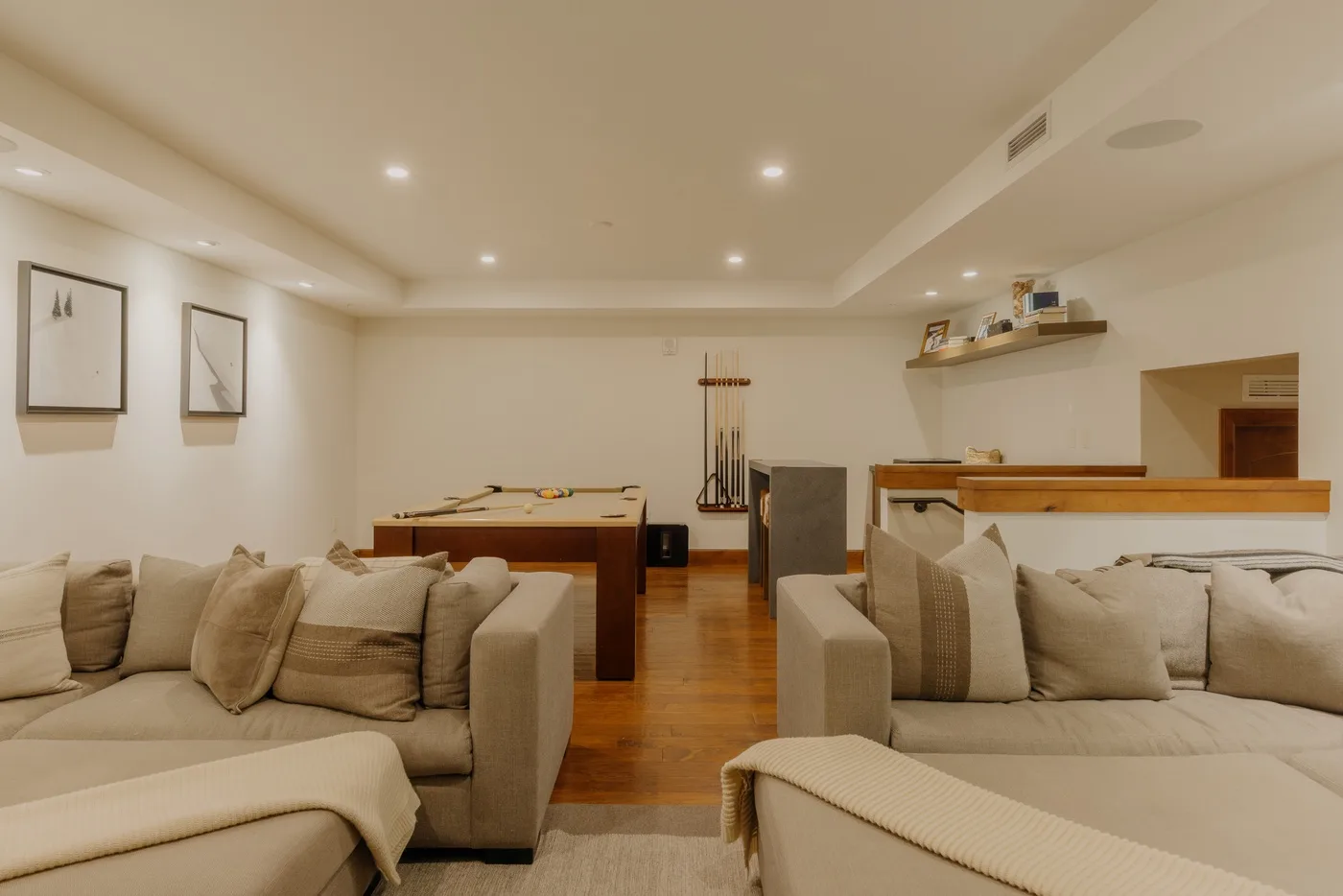 A living room with seating, a pool table, and warm wood flooring.