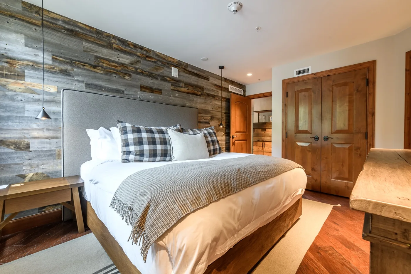 A bedroom with a large bed, plaid pillows, and a wood-paneled accent wall.
