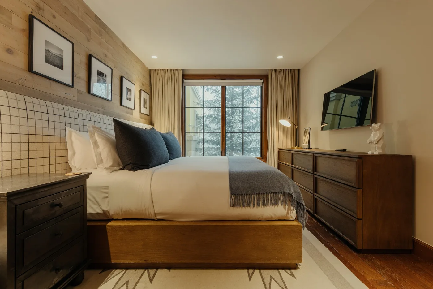 A bedroom with a neatly made bed, framed prints, and a large window.