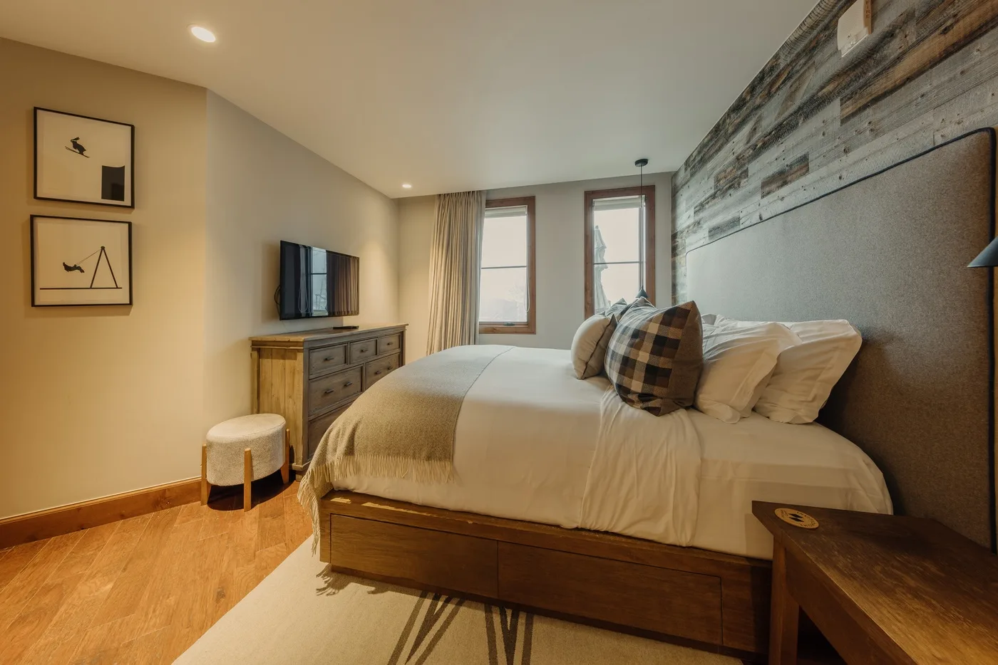 A bedroom with a large bed, bedside table, and two windows.