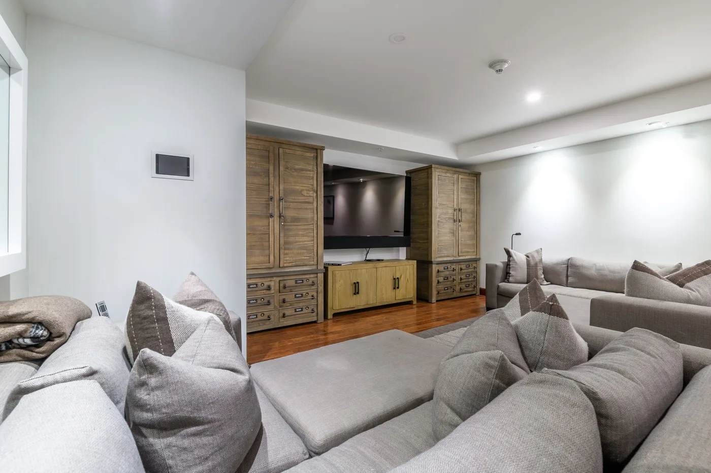Living room with gray seating arranged around a television and wooden cabinets.