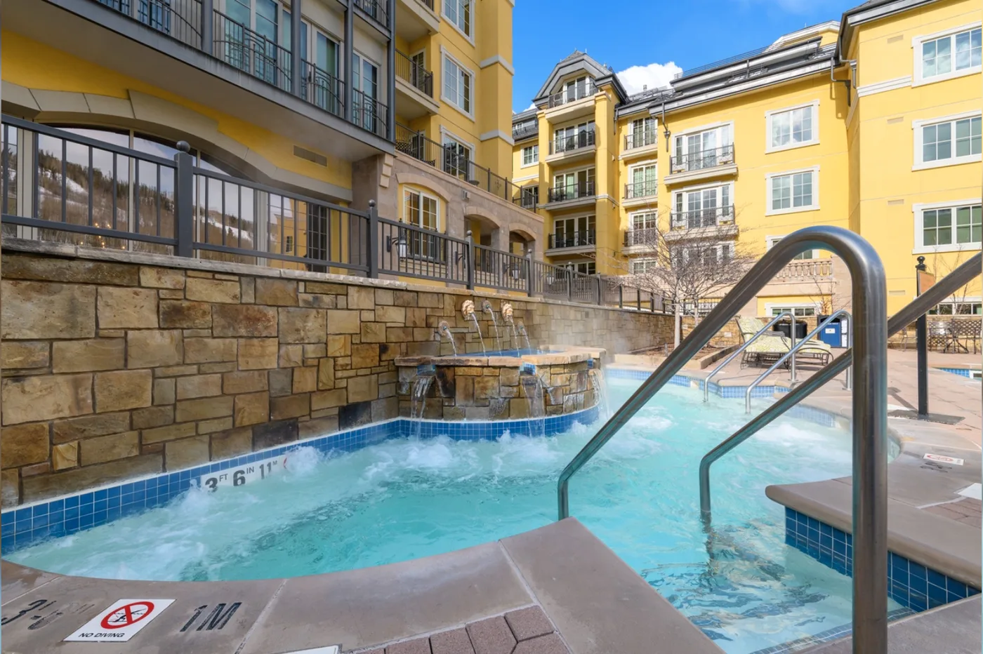 An outdoor swimming pool sits beside yellow multi-story buildings.