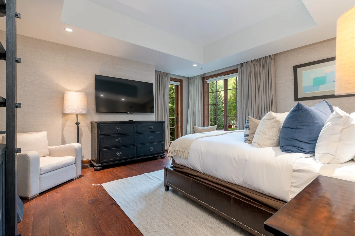 A bedroom with a neatly made bed, a television, and a light rug.