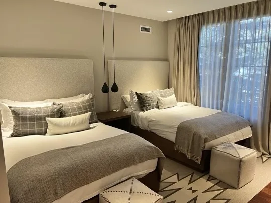 A bedroom with two beds, pendant lights, and a large curtained window.