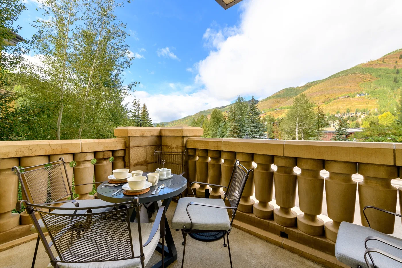 A balcony seating area with a small table overlooks a green hillside.