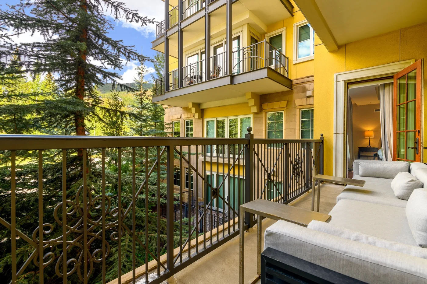 A furnished balcony overlooks trees and the neighboring building.
