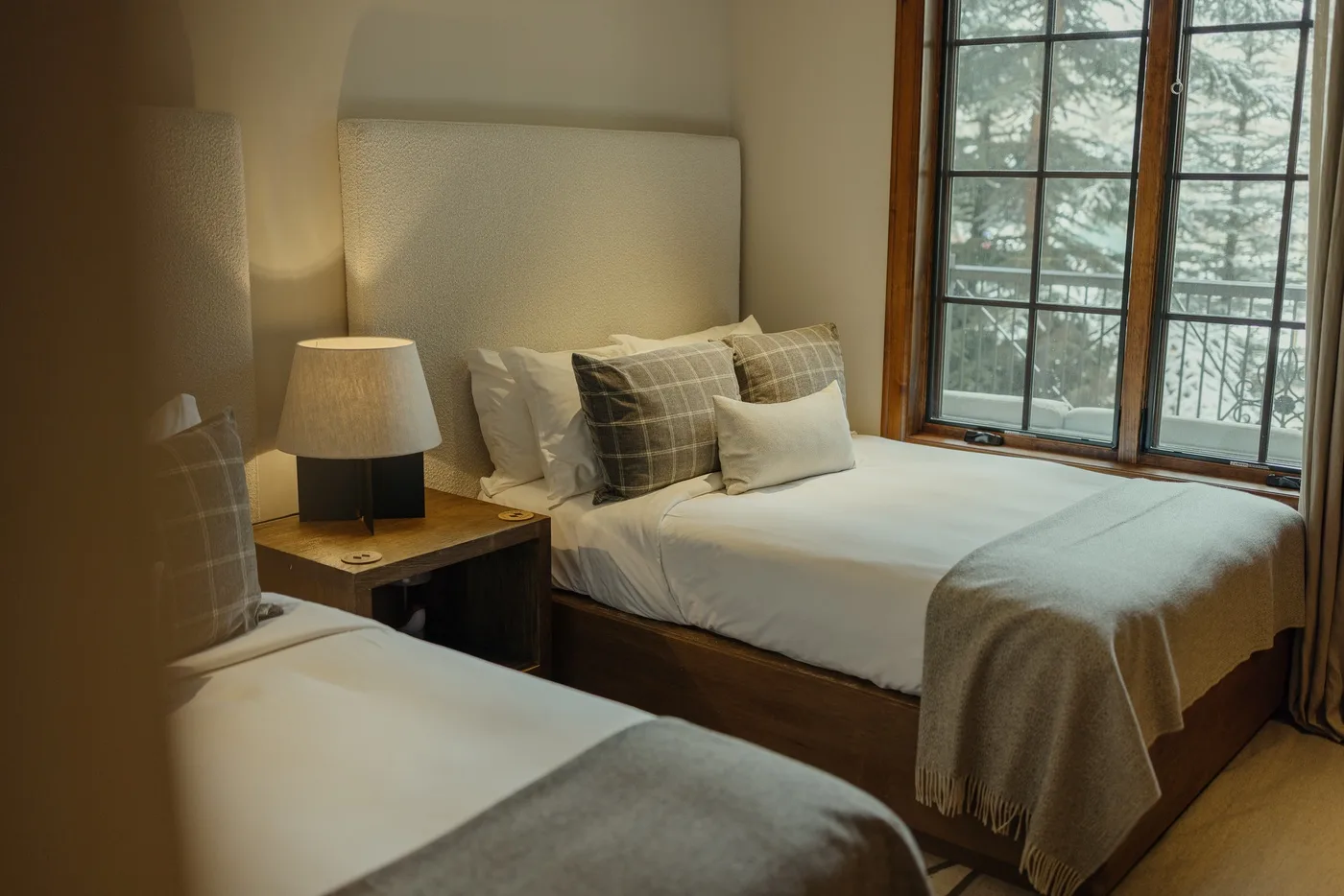 A bedroom with two beds, bedside lighting, and a large window.