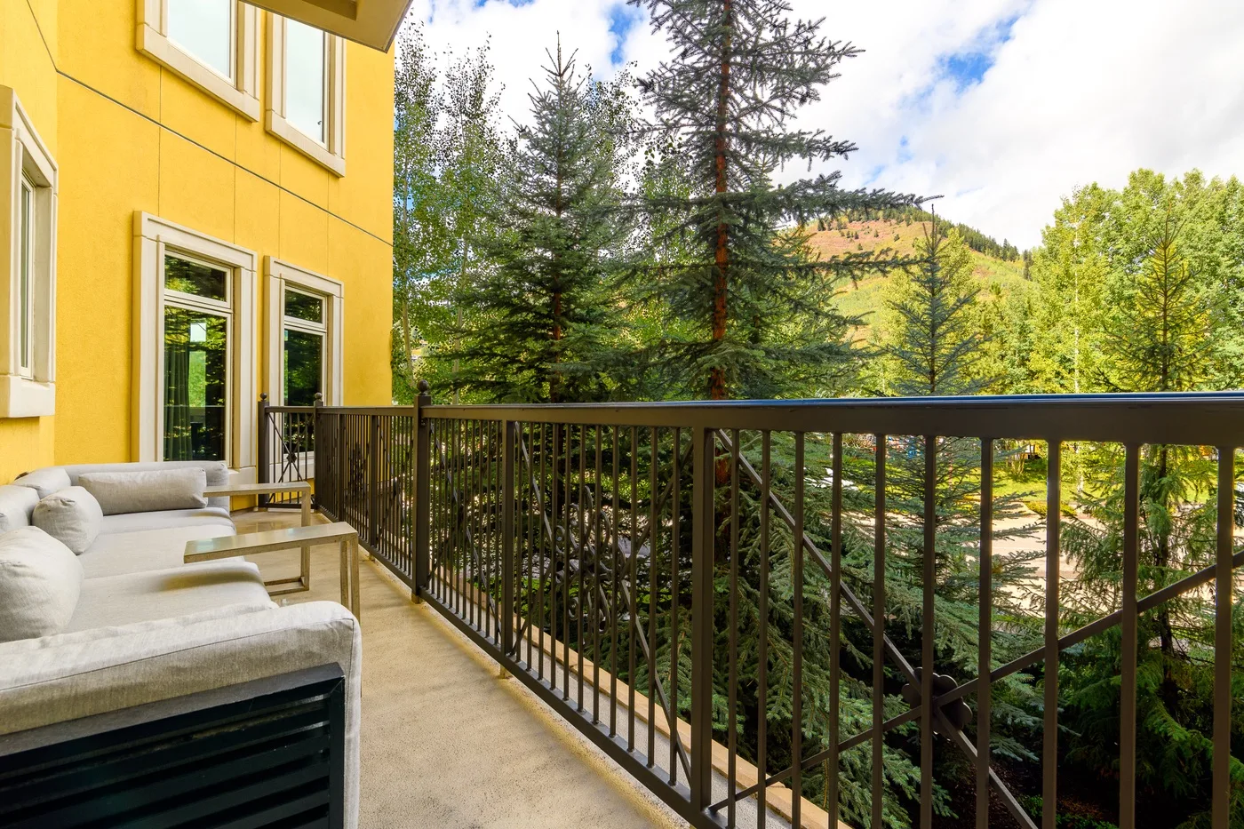 A balcony with outdoor seating overlooks trees and a wooded hillside.