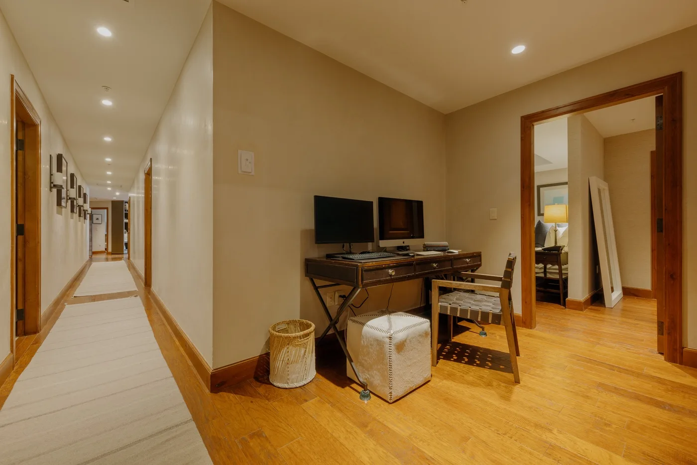 A desk with monitors sits beside a hallway and an open doorway.