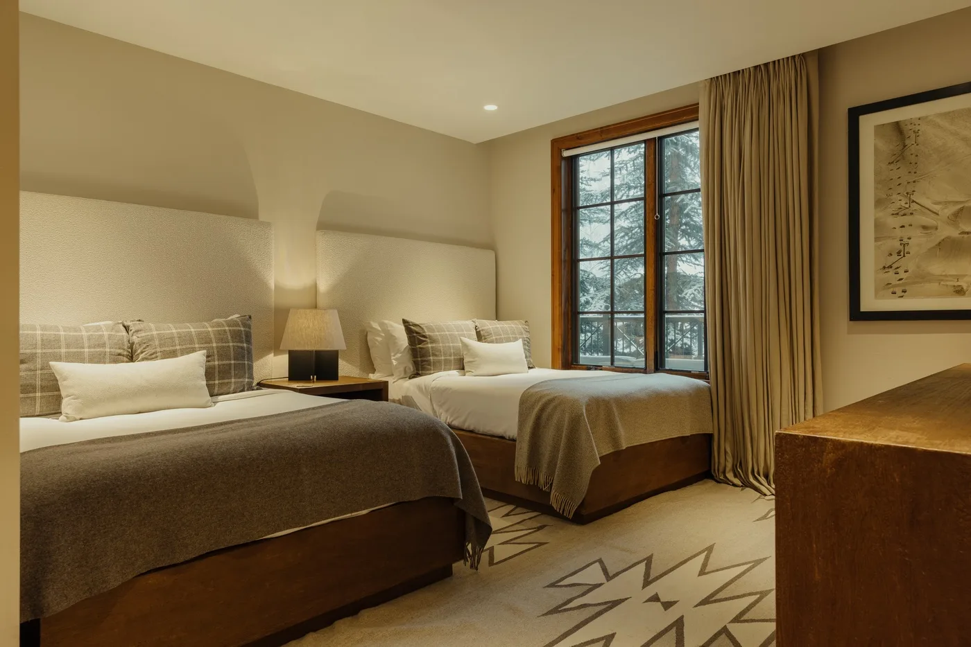 A bedroom with two beds, a bedside lamp, and a curtained window.