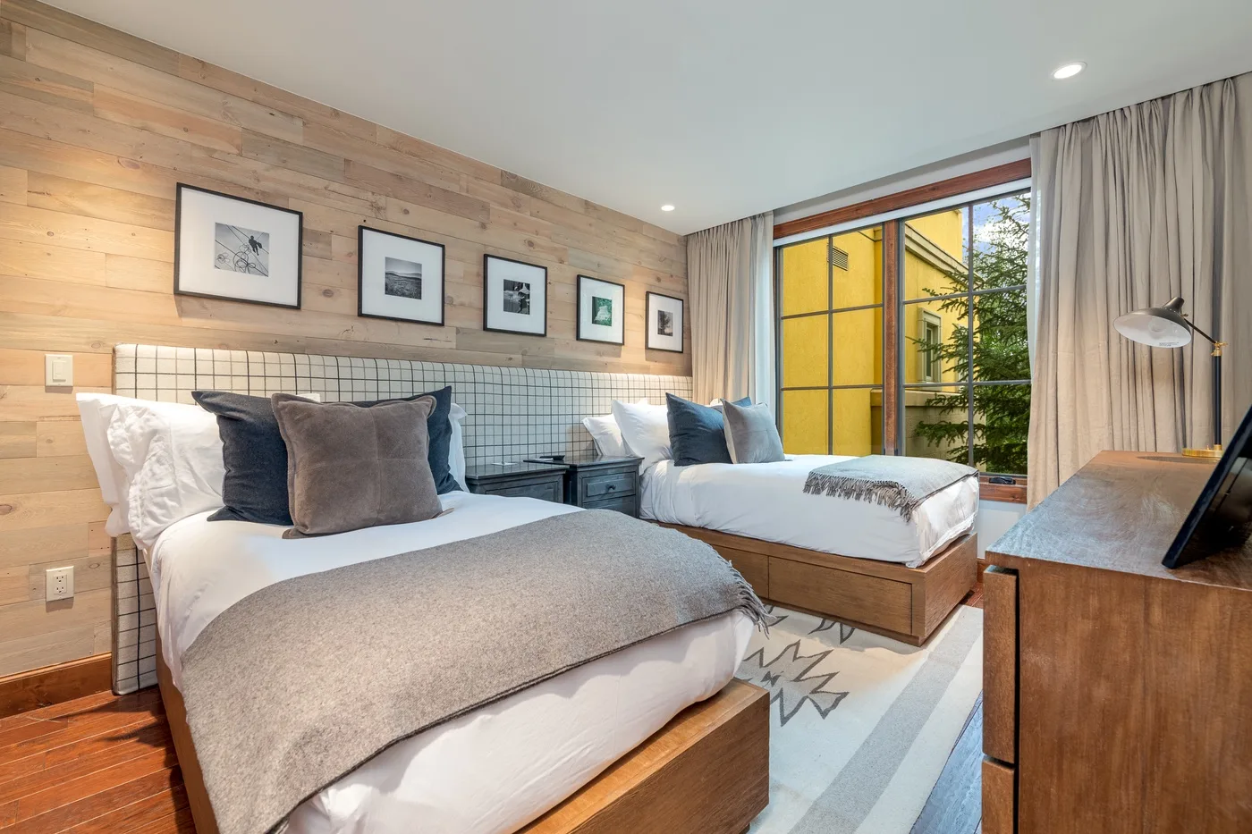A bedroom with two beds, framed pictures, and a large window.